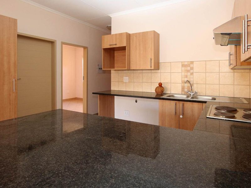 A functional kitchen featuring granite countertops, built-in cabinetry, an electric hob with extractor fan, and a tiled backsplash.