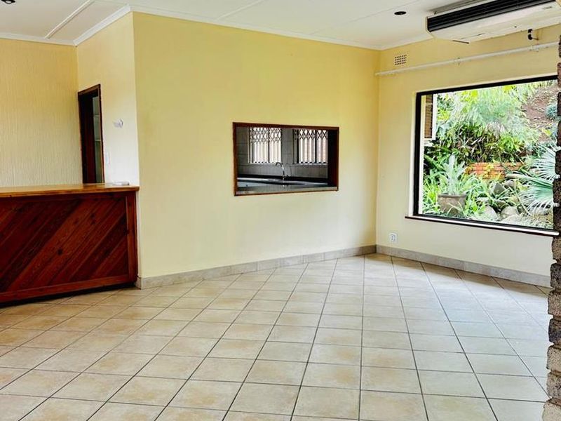 Spacious living area featuring tiled flooring, recessed lighting, a built-in wooden bar, and a serving hatch connecting to the kitchen area.