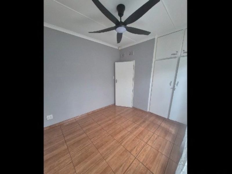 A clean, empty bedroom featuring tiled flooring, built-in cupboards, and a ceiling fan, offering a neutral canvas for personalization.
