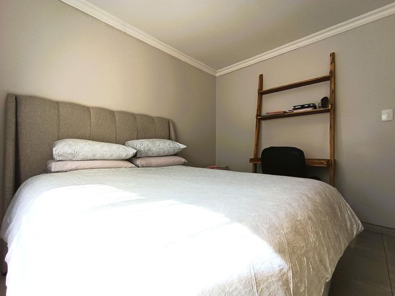 A well-maintained bedroom featuring neutral wall tones, crown molding, and tiled flooring, providing a clean and comfortable living space.