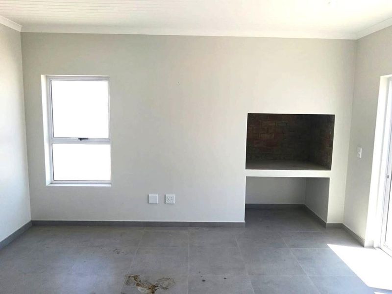 An empty living area featuring neutral wall finishes, tiled flooring, and a built-in brick fireplace, offering a clean canvas for interior design.