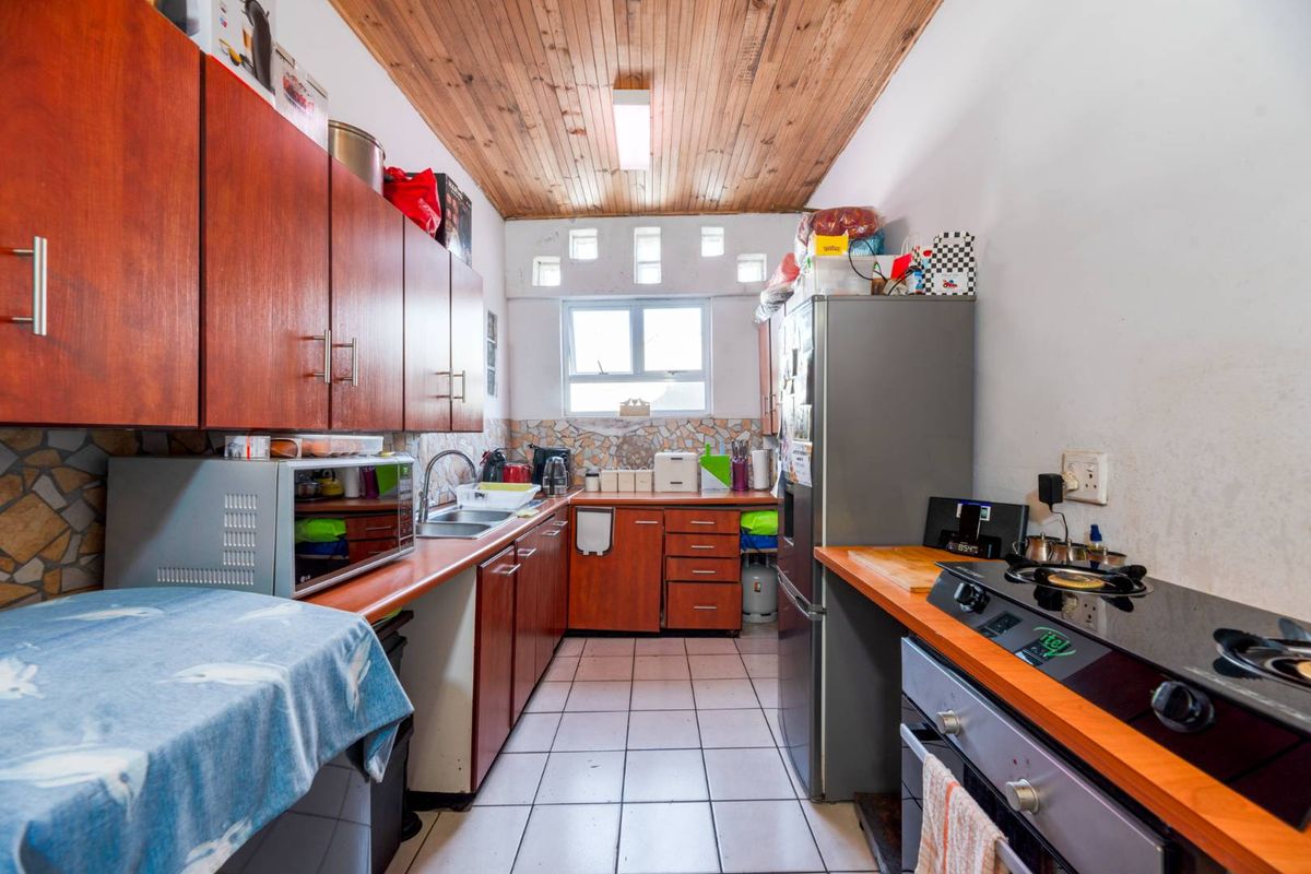 A functional galley-style kitchen featuring wood-look cabinetry, tiled splashbacks, a built-in oven with hob, and a timber-paneled ceiling.