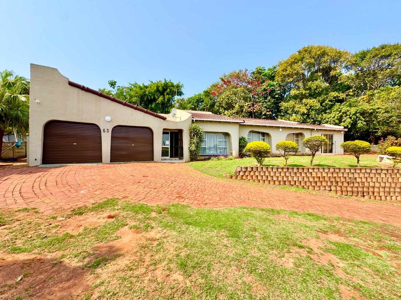 Front elevation of a single-story house featuring a double garage, paved driveway, and a terraced garden with a retaining wall.