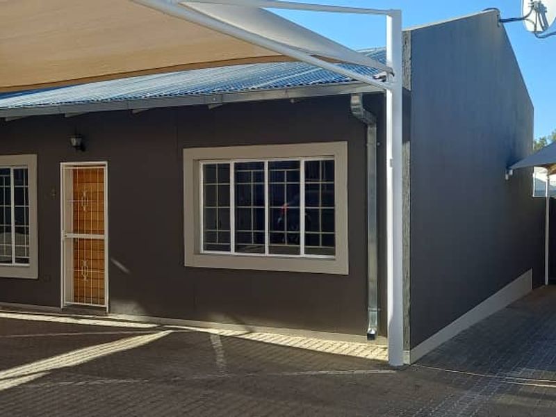Front exterior view of a townhouse featuring a paved driveway, shade sail covering, and secure window burglar bars.