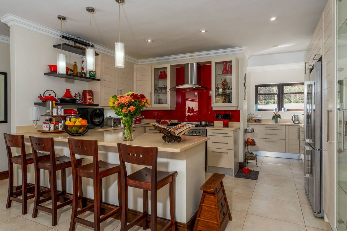 Modern kitchen featuring a breakfast bar, stone countertops, red glass splashback, stainless steel extractor fan, and ample cabinetry with integrated appliance space.
