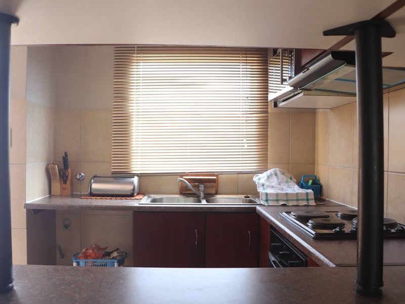 A functional kitchen featuring dark veneer cabinetry, laminate countertops, a double sink, and a built-in hob with an extractor fan.