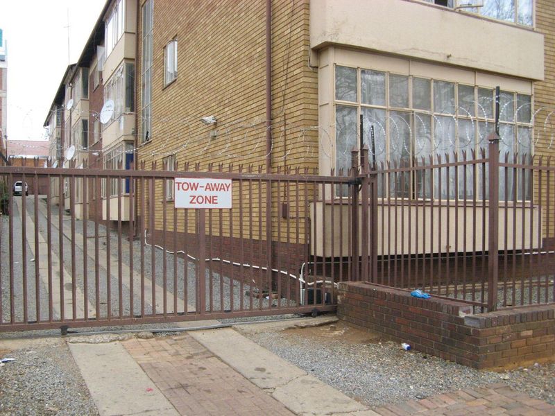 Exterior view of an apartment building featuring a brick facade, metal security gate, and perimeter security fencing with razor wire.