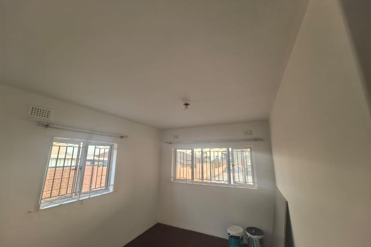 A clean, empty bedroom featuring white walls, casement windows with security bars, and simple ceiling lighting, ready for personalization.