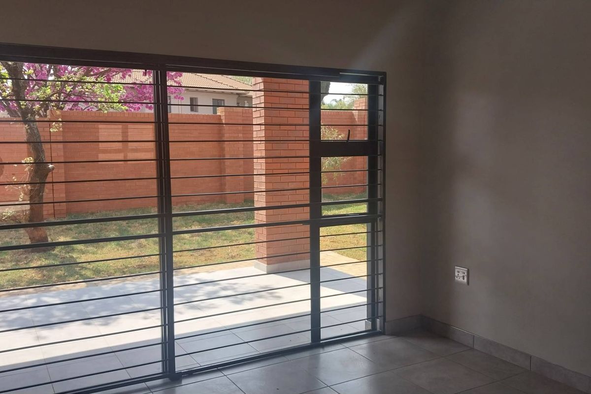 An empty living room featuring tiled floors and a large sliding glass door with security bars, providing direct access to the rear patio and garden.