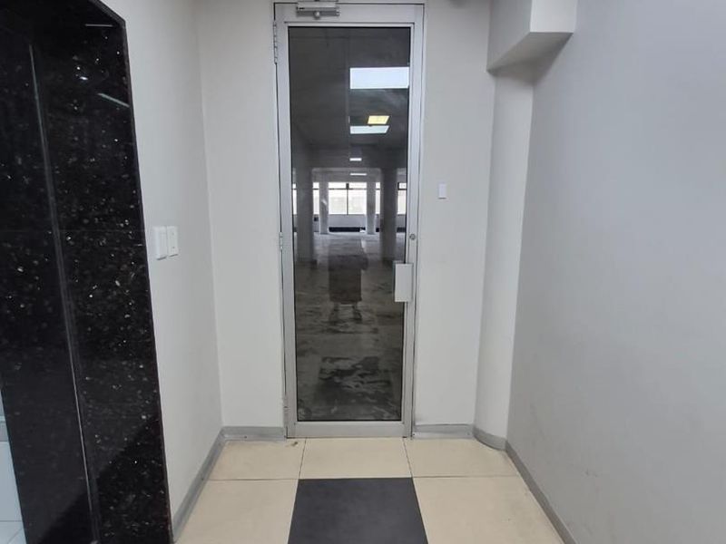 An office entrance area featuring a glass door, tiled flooring, and granite wall accents, leading into an open-plan workspace.
