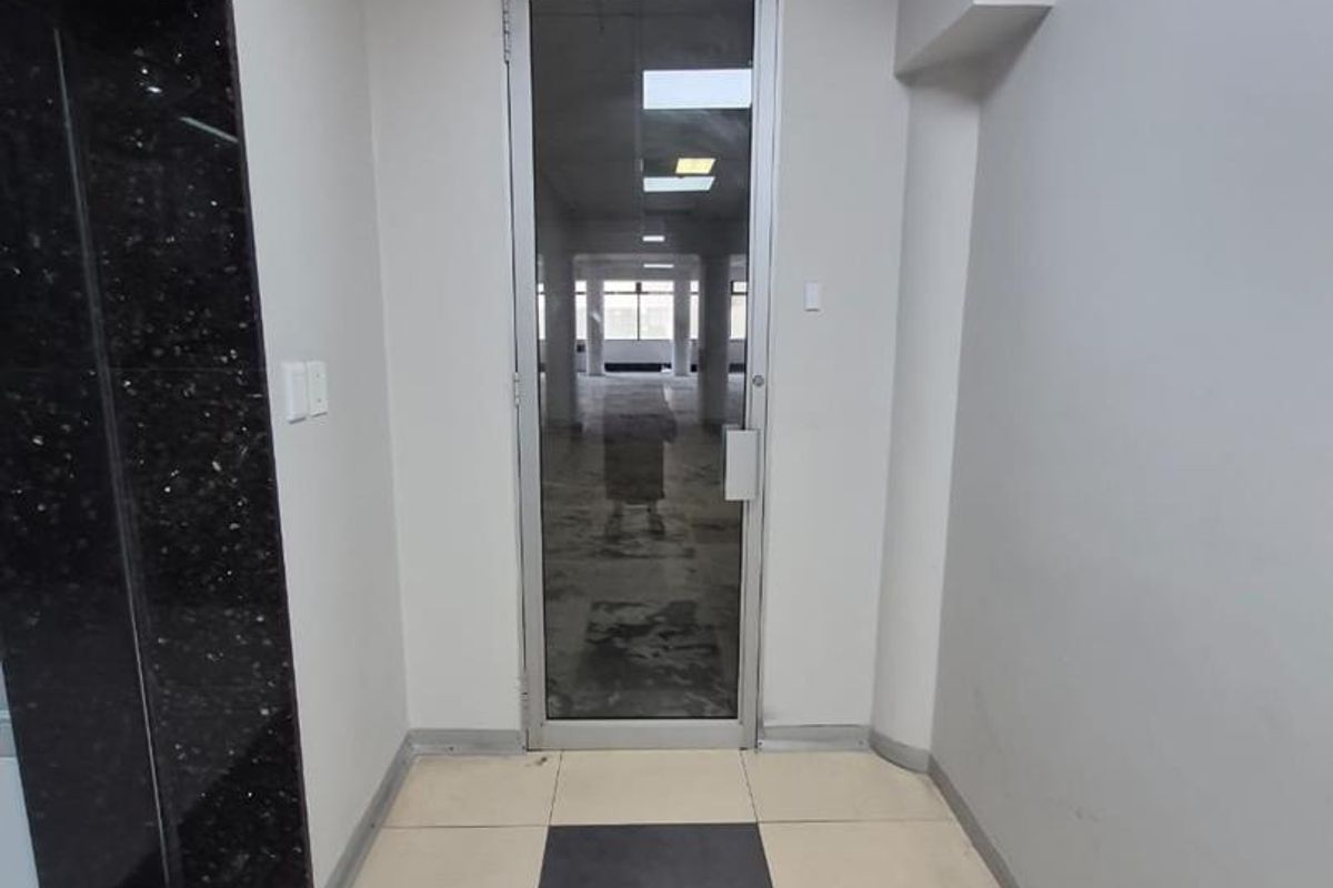 An office entrance area featuring a glass door, tiled flooring, and granite wall accents, leading into an open-plan workspace.