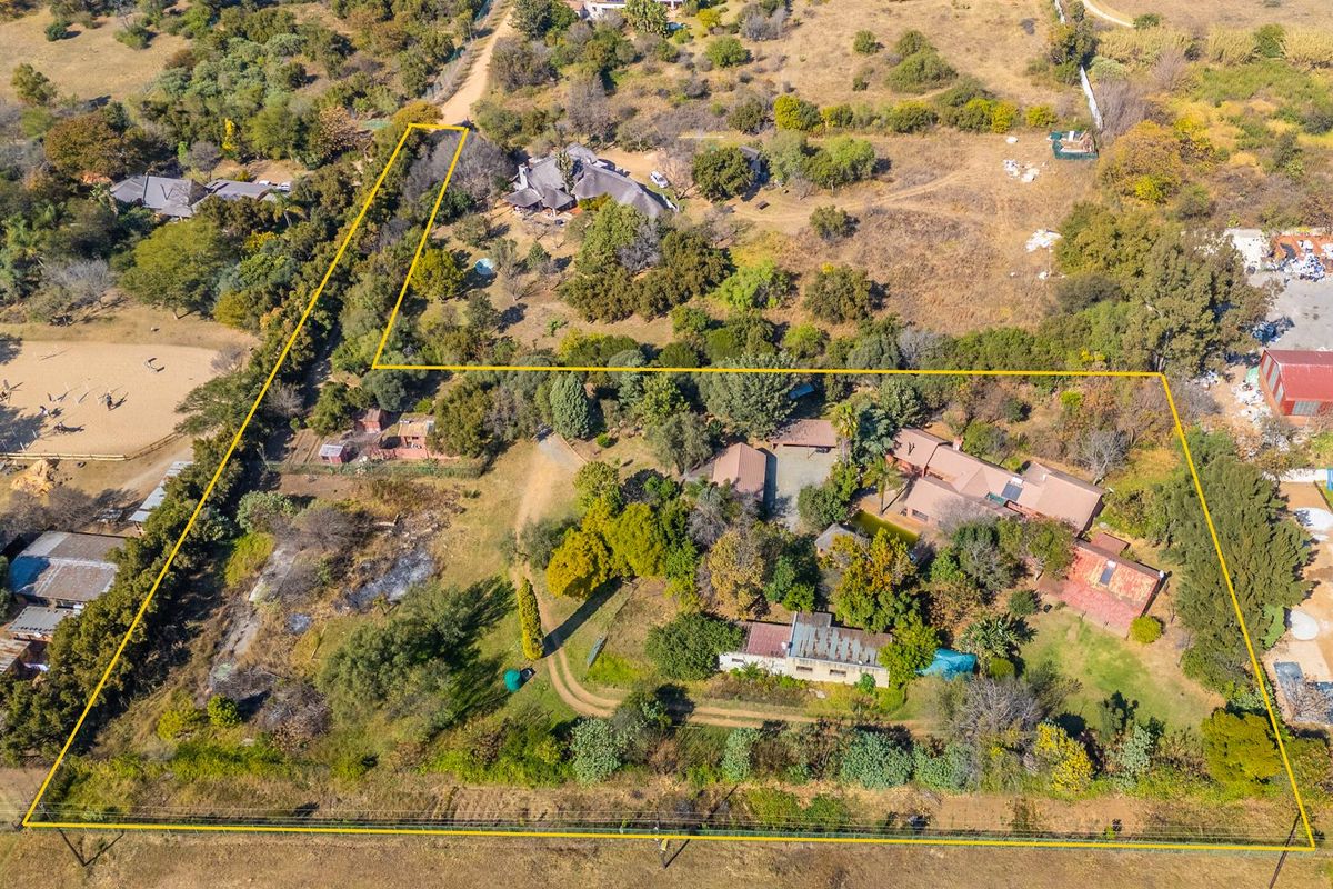 Aerial view of a large small holding property featuring multiple structures, extensive grounds, and established trees within a rural setting.