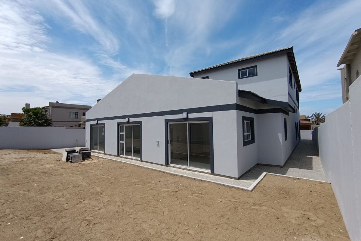 Rear view of a modern two-story house featuring sliding glass doors, paved walkways, and an expansive, undeveloped backyard area.