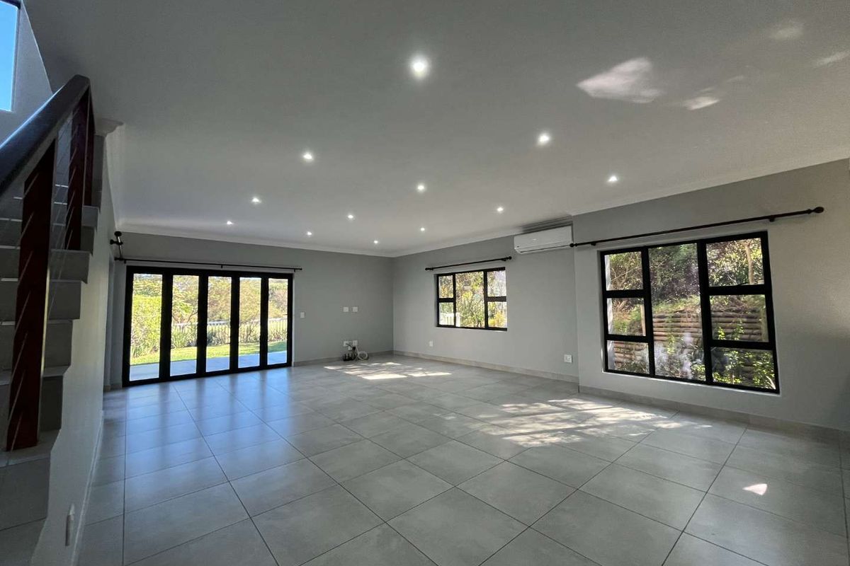 Spacious, light-filled living area featuring neutral tiled floors, recessed downlighting, split-system air conditioning, and large aluminium-framed windows and stacker doors leading outdoors.