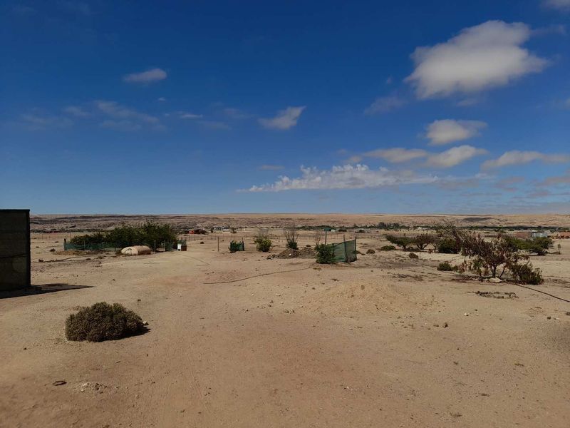 Expansive view of the arid small holding landscape featuring open terrain, sparse vegetation, and perimeter fencing under a clear blue sky.