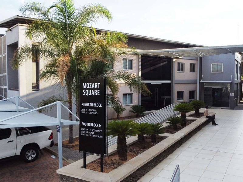 Exterior view of Mozart Square office complex featuring modern architecture, paved walkways, covered parking, and clear directional signage for tenants.