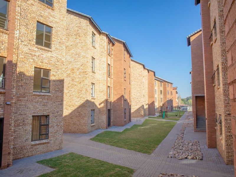 A view of the apartment complex exterior featuring face brick facades, paved walkways, and well-maintained communal lawn areas between the residential blocks.
