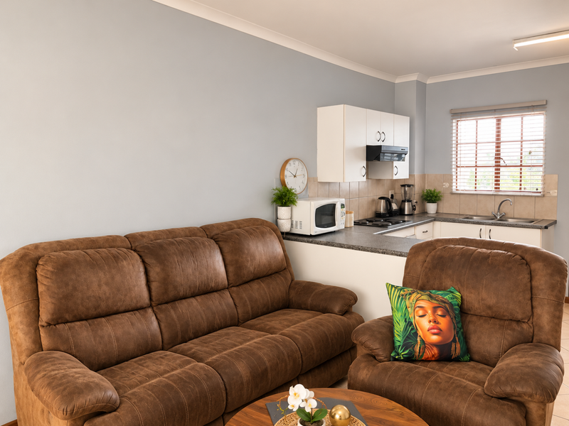 Open plan living area featuring a compact kitchen with built-in cabinetry, laminate countertops, and a tiled backsplash, seamlessly connected to the lounge space.