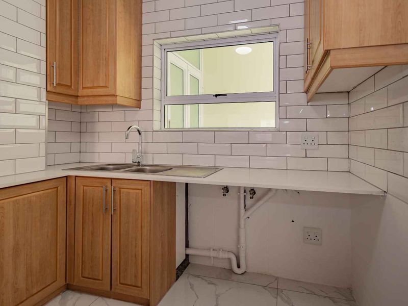 A clean, modern kitchen featuring wooden cabinetry, white subway tile backsplash, and marble-look floor tiles, with an open space for under-counter appliances.