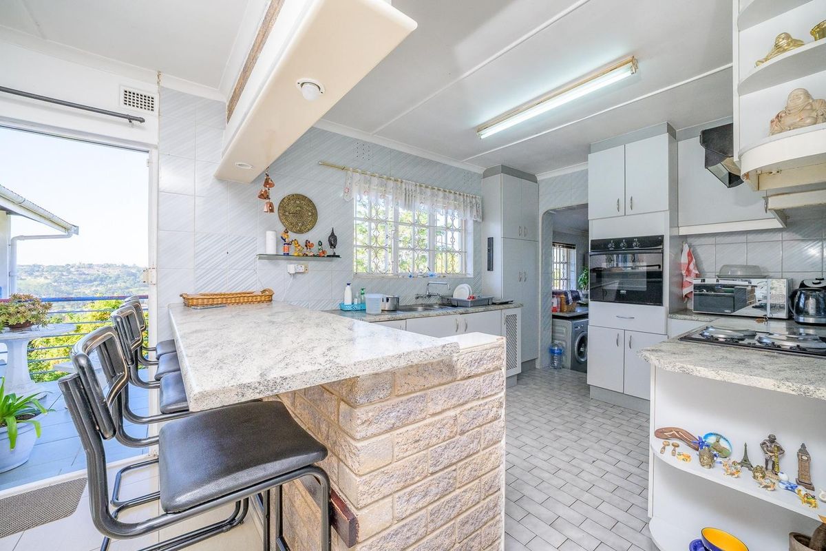 Functional kitchen featuring a brick-base breakfast bar, built-in oven, gas hob, and tiled finishes, with direct access to an outdoor balcony area.