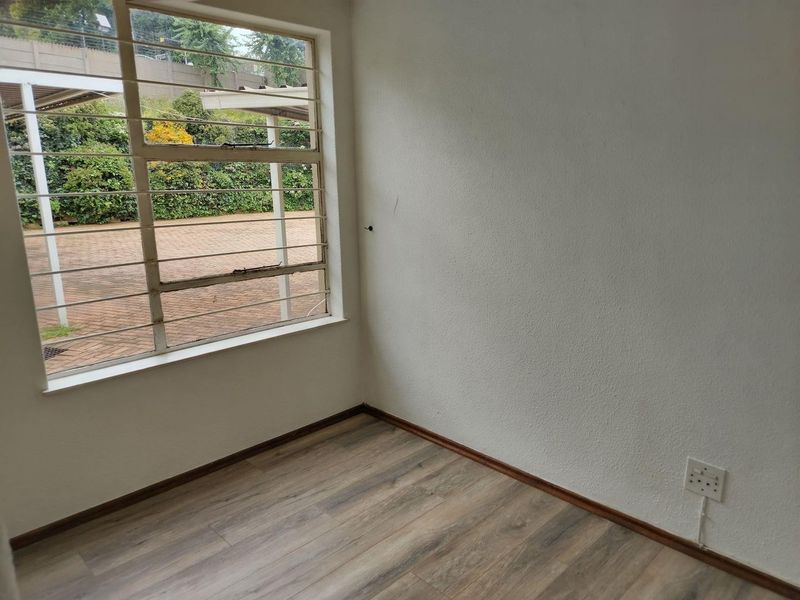 A bright, empty bedroom featuring modern laminate flooring, large windows with security bars, and neutral walls, ready for personalization.