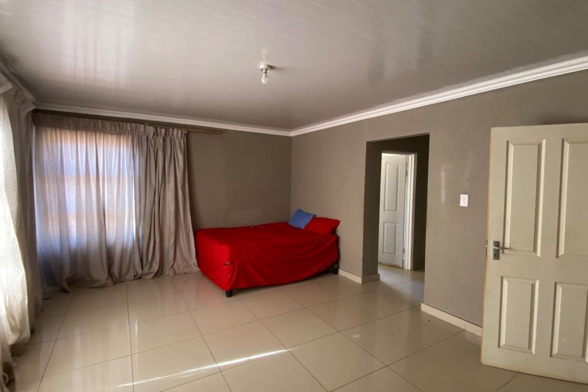 A spacious bedroom featuring neutral tiled flooring, crown molding, and a large window with curtain tracks, offering a blank canvas for personalization.