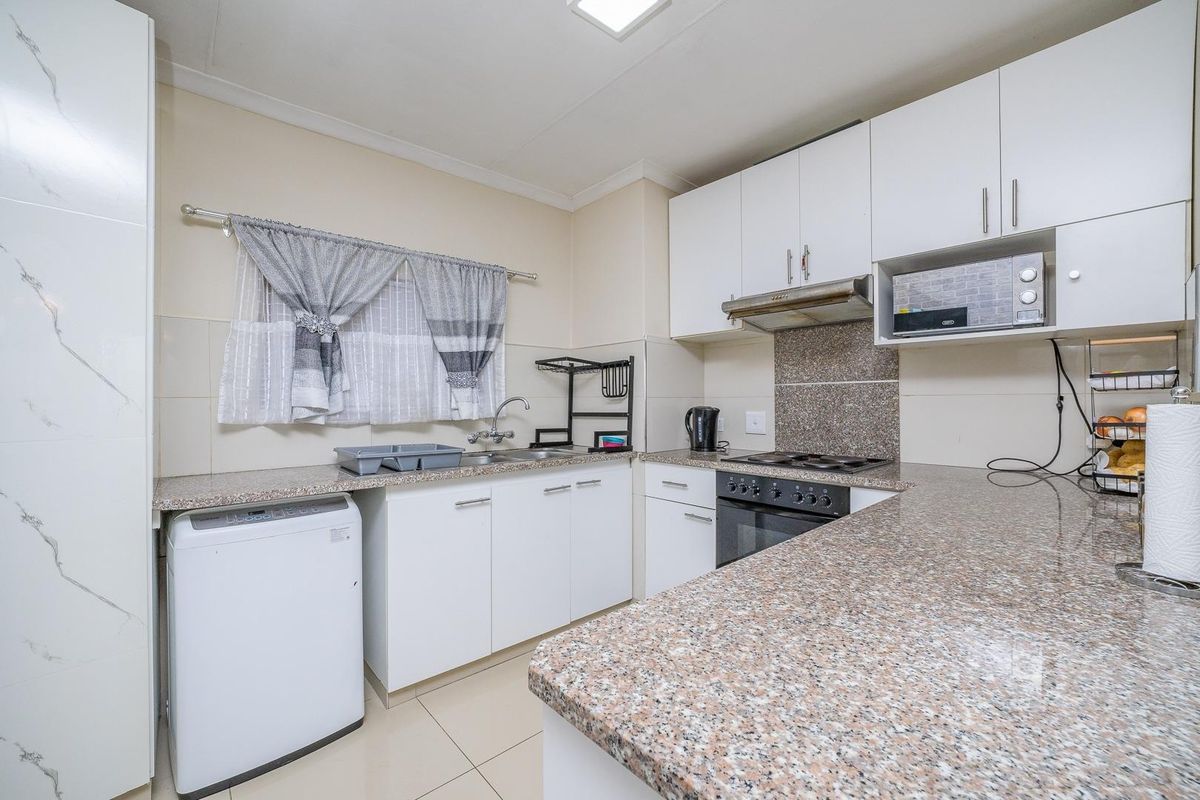 A functional kitchen featuring granite countertops, built-in oven, hob, extractor fan, and ample cabinetry, providing a practical and well-maintained cooking space.