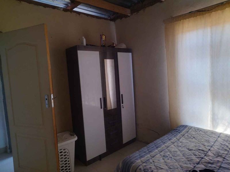A bedroom featuring unfinished ceiling and exposed roof structure, requiring cosmetic repairs and finishing to improve the overall condition.
