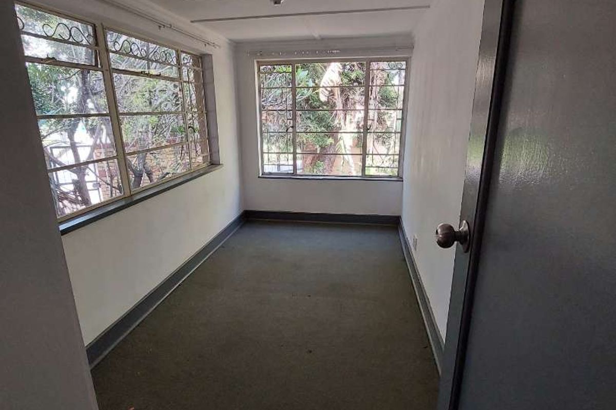An empty bedroom featuring steel-framed windows, carpeted flooring, and surface-mounted electrical conduit, offering a blank canvas for renovation.