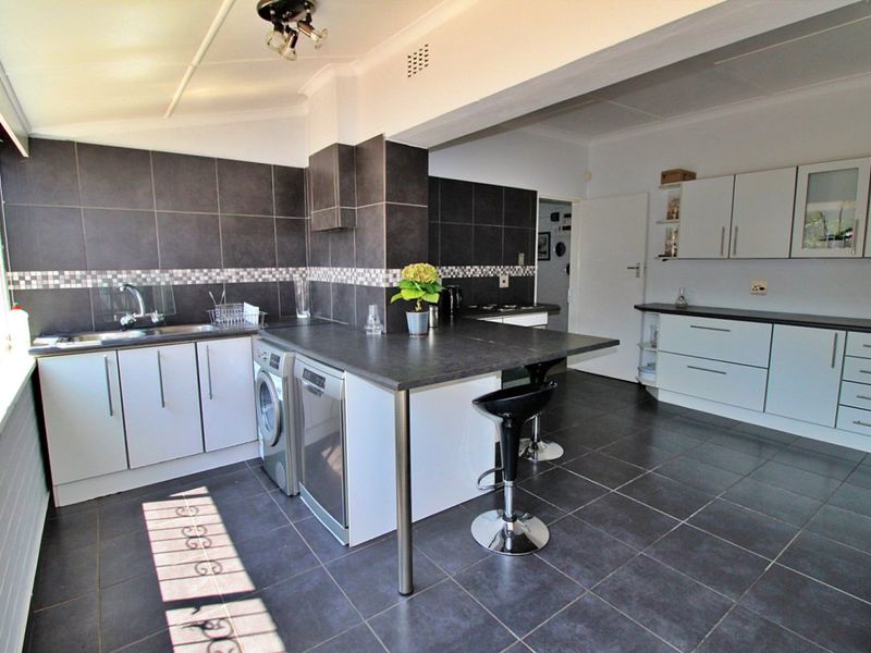 A functional kitchen featuring dark tiled flooring, contrasting cabinetry, a breakfast bar, and integrated workspace with a tiled backsplash.