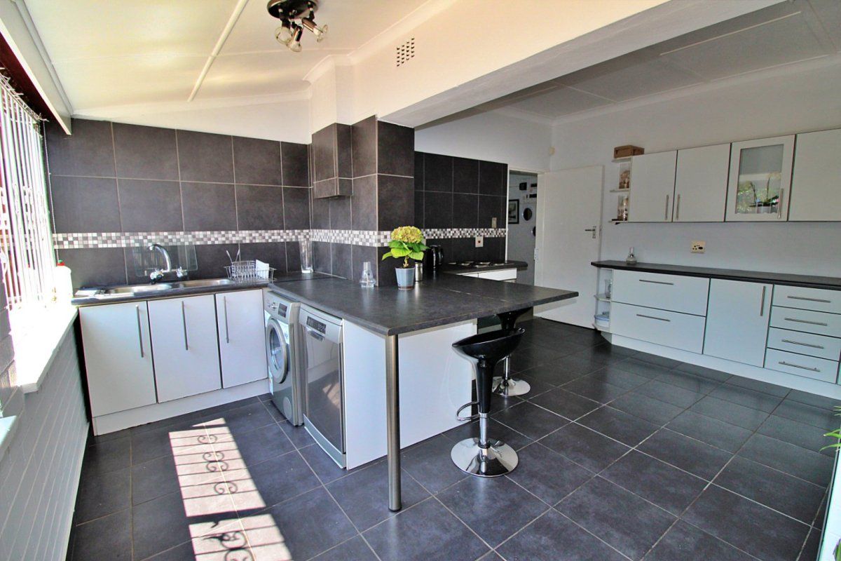 A functional kitchen featuring dark tiled flooring, contrasting cabinetry, a breakfast bar, and integrated workspace with a tiled backsplash.