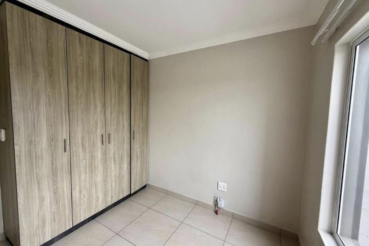 A clean, empty bedroom featuring neutral tiled flooring, modern wood-finish built-in cupboards, and crisp white walls with ceiling cornicing.
