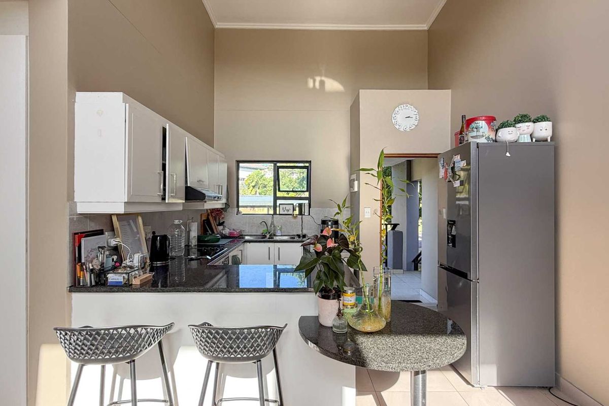 A functional kitchen featuring granite countertops, white cabinetry, a breakfast bar, and a double sink, with high ceilings and natural light.