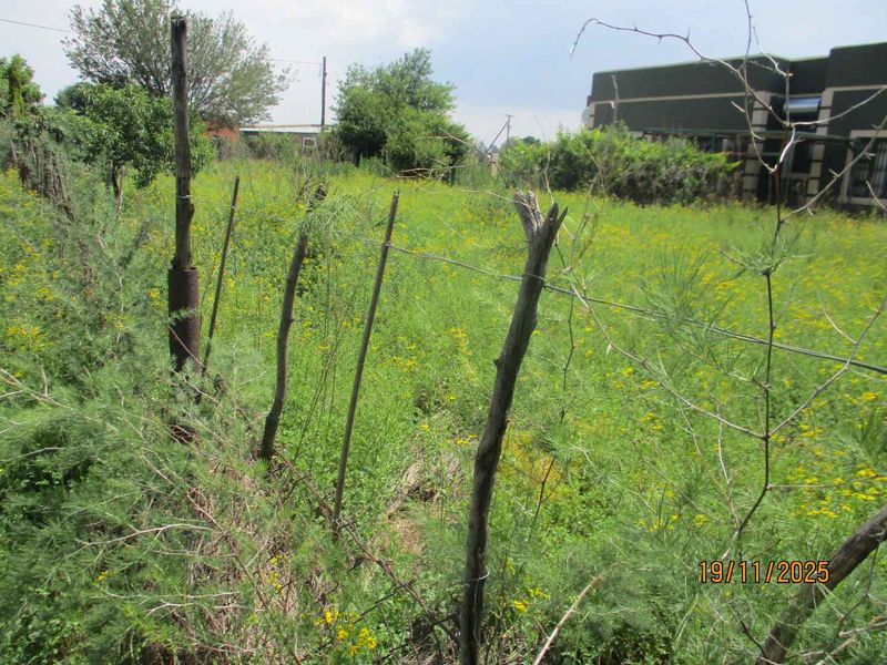 A view of a vacant residential plot featuring overgrown vegetation and basic wire fencing with wooden posts.