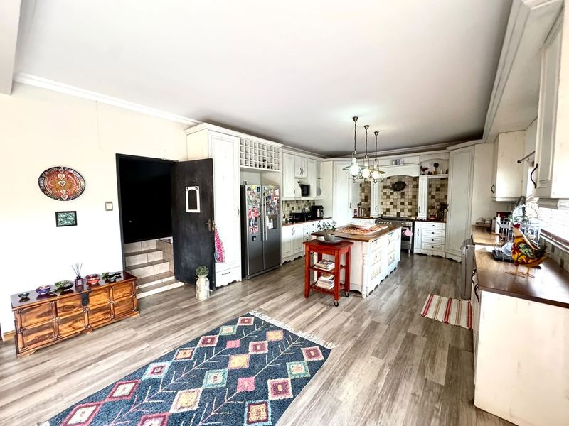 Spacious kitchen featuring white cabinetry, a central island, tiled backsplash, and wood-look laminate flooring, offering a functional and inviting culinary space.
