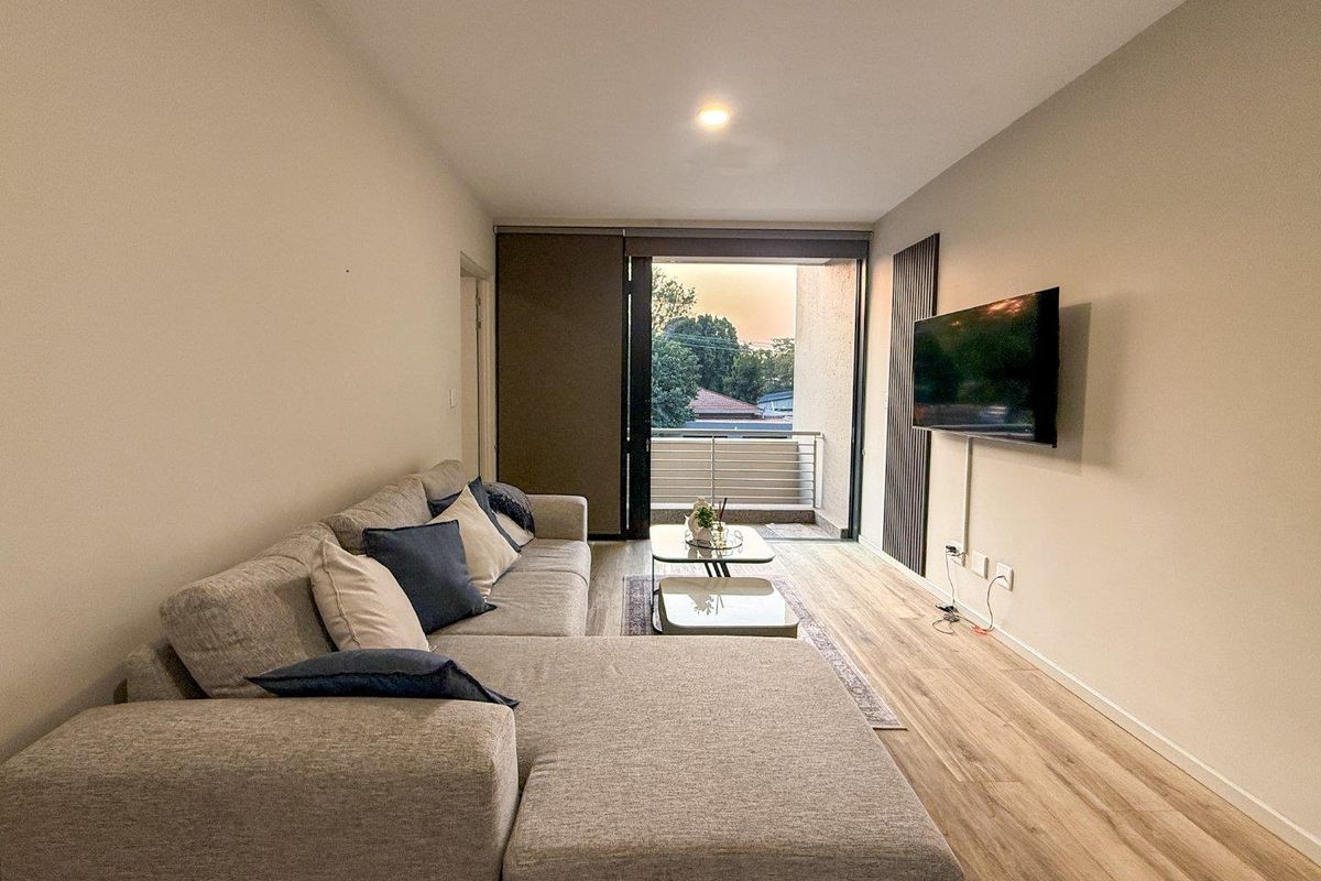 Modern living room featuring laminate flooring, recessed lighting, and direct access to a private balcony through a sliding glass door.