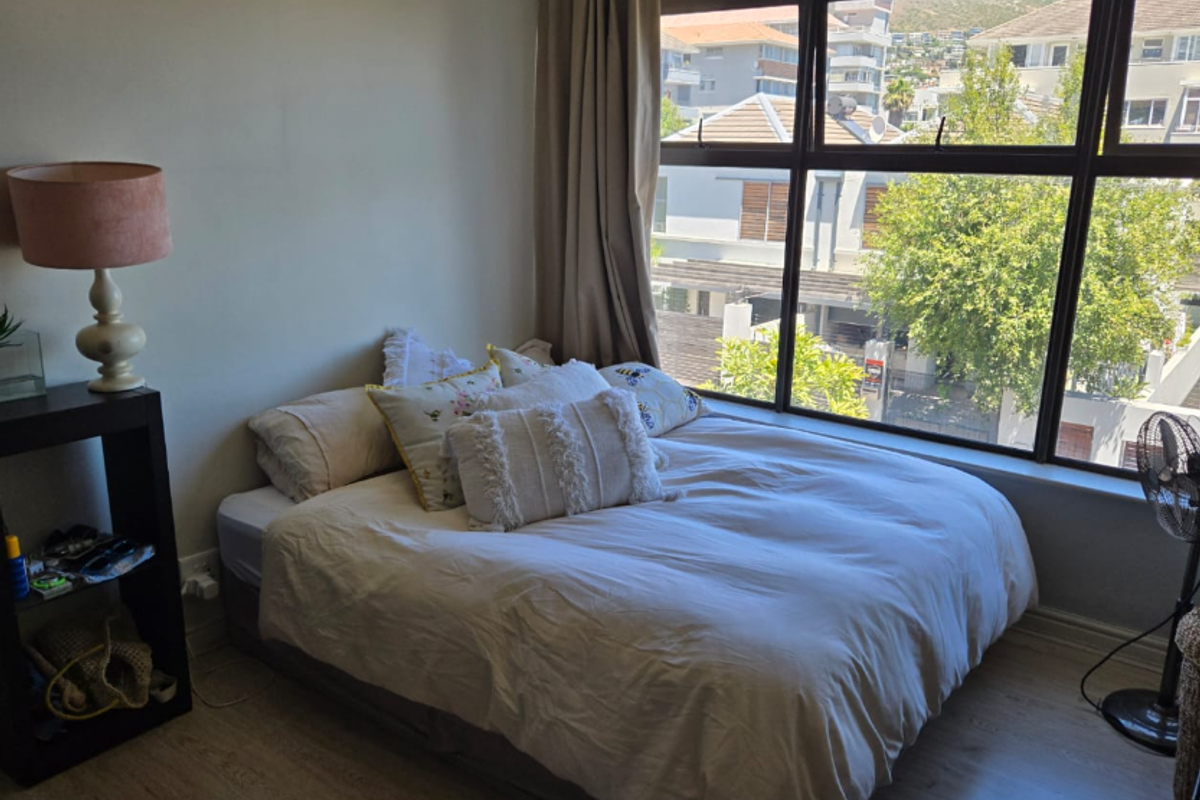A bedroom featuring laminate flooring and a large window providing natural light and a view of the surrounding neighborhood.