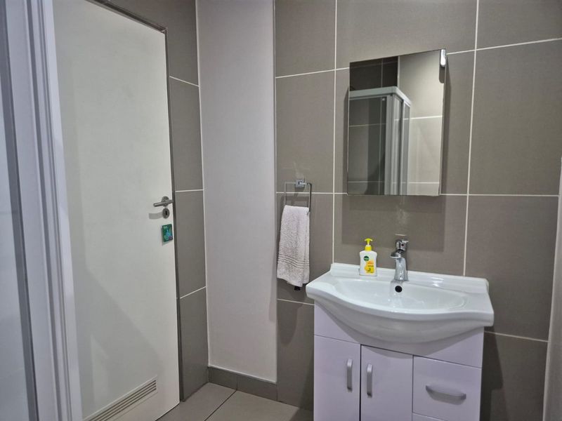 Modern bathroom featuring a vanity cabinet with basin, chrome mixer tap, wall-mounted mirror, and neutral tiled finishes.