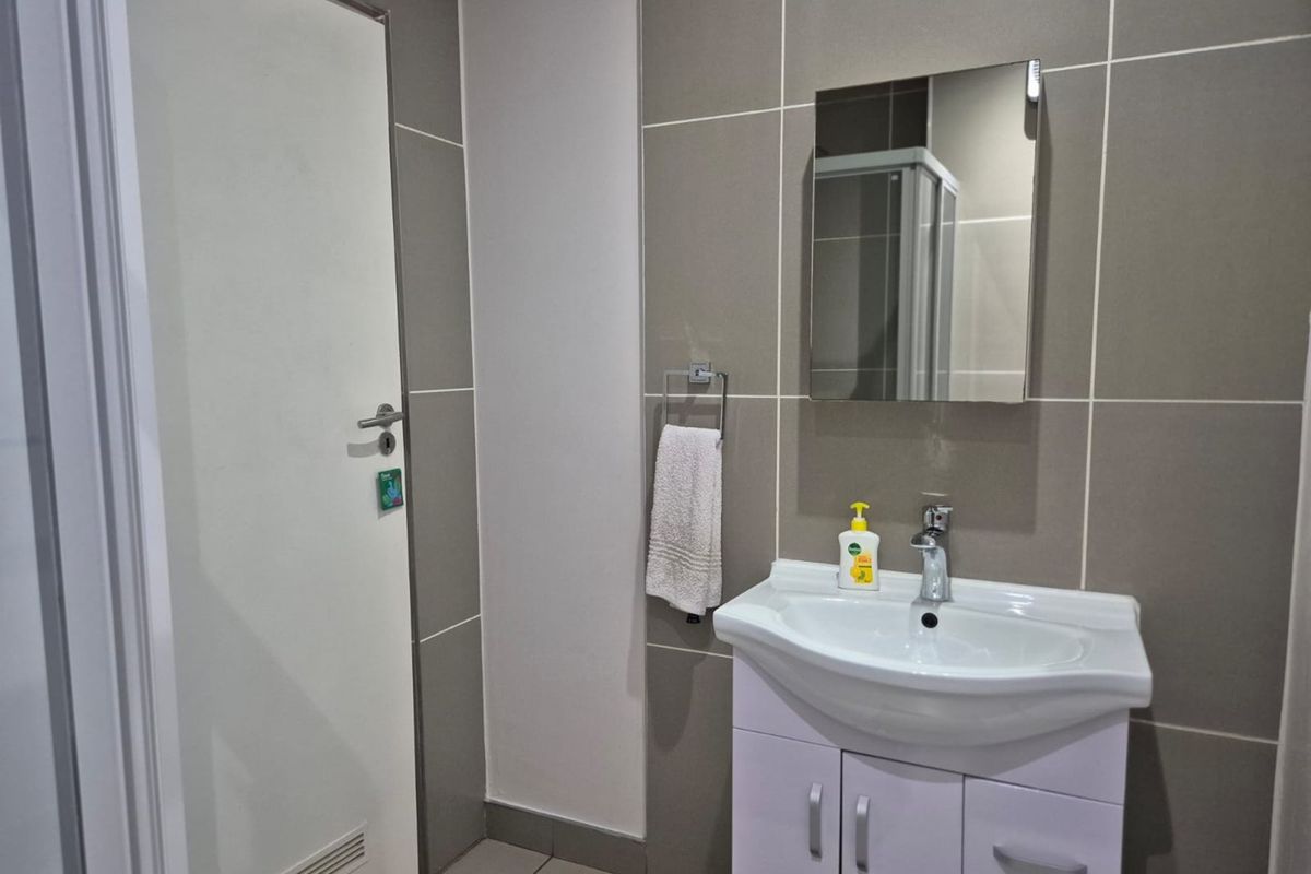 Modern bathroom featuring a vanity cabinet with basin, chrome mixer tap, wall-mounted mirror, and neutral tiled finishes.