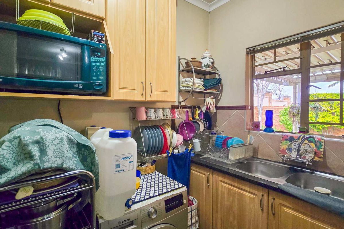 A functional kitchen area featuring wooden cabinetry, a double basin sink, and a tiled splashback, providing practical workspace and storage.