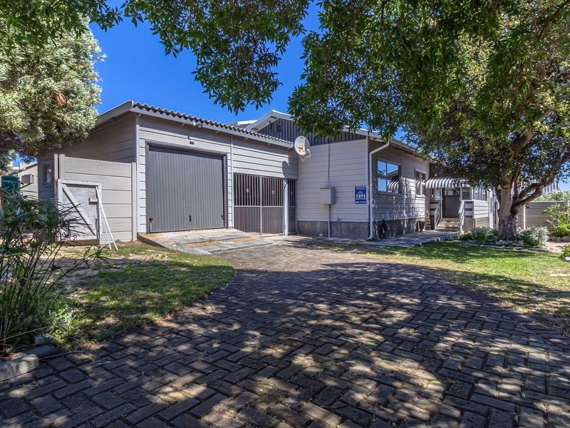 Front view of the property featuring a paved driveway, single garage, and established garden area with mature trees.