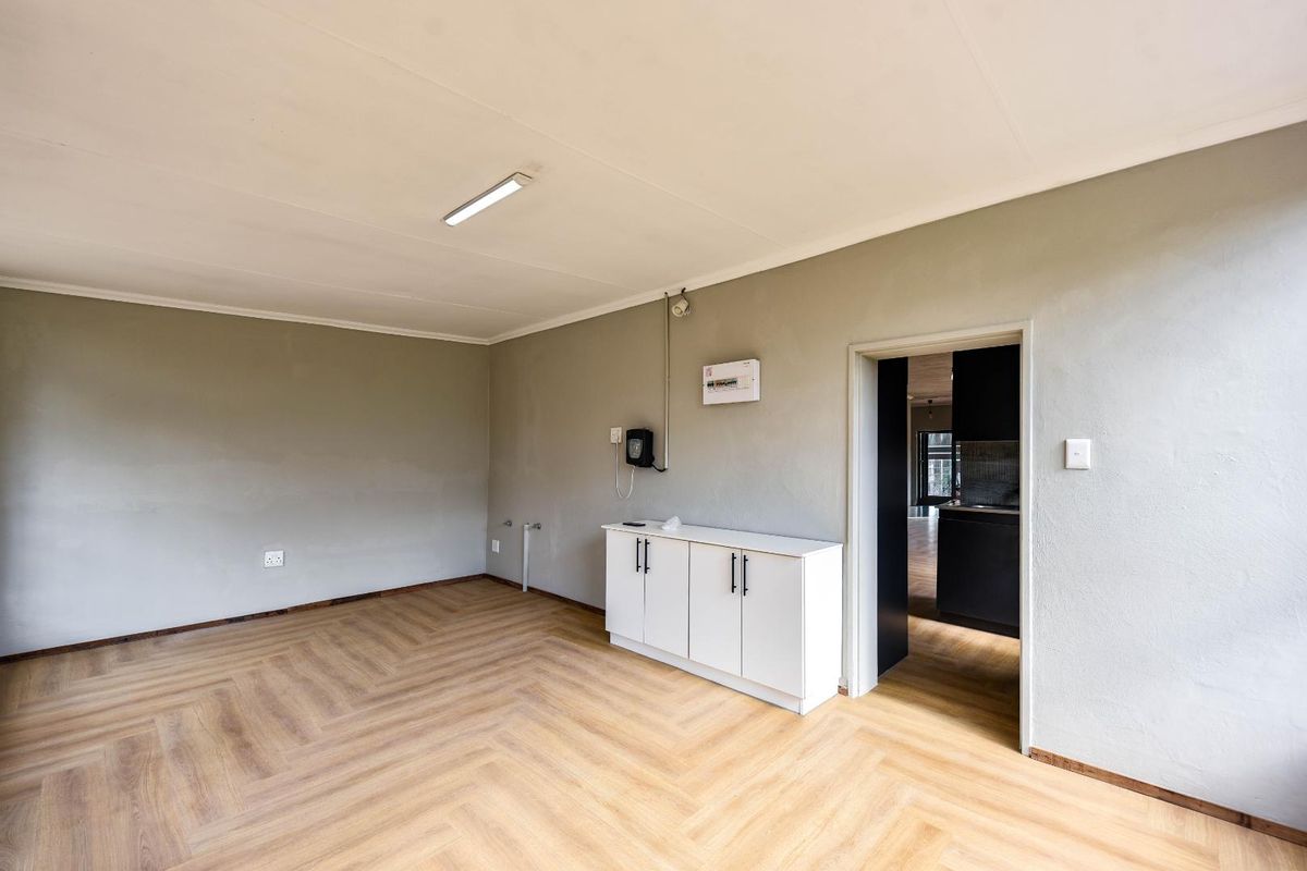A bright, empty living area featuring light wood-look herringbone flooring and a built-in white storage cabinet, with direct access to the kitchen.