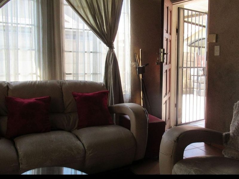 A living room area featuring tiled flooring, large windows for natural light, and direct access to an exterior space through a timber door with security gate.