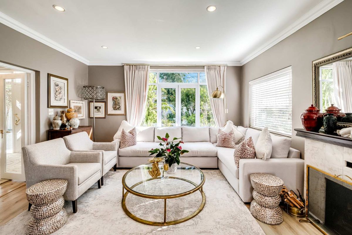 A well-appointed living room featuring hardwood flooring, crown molding, recessed lighting, and a classic marble fireplace surround with garden views through french doors.