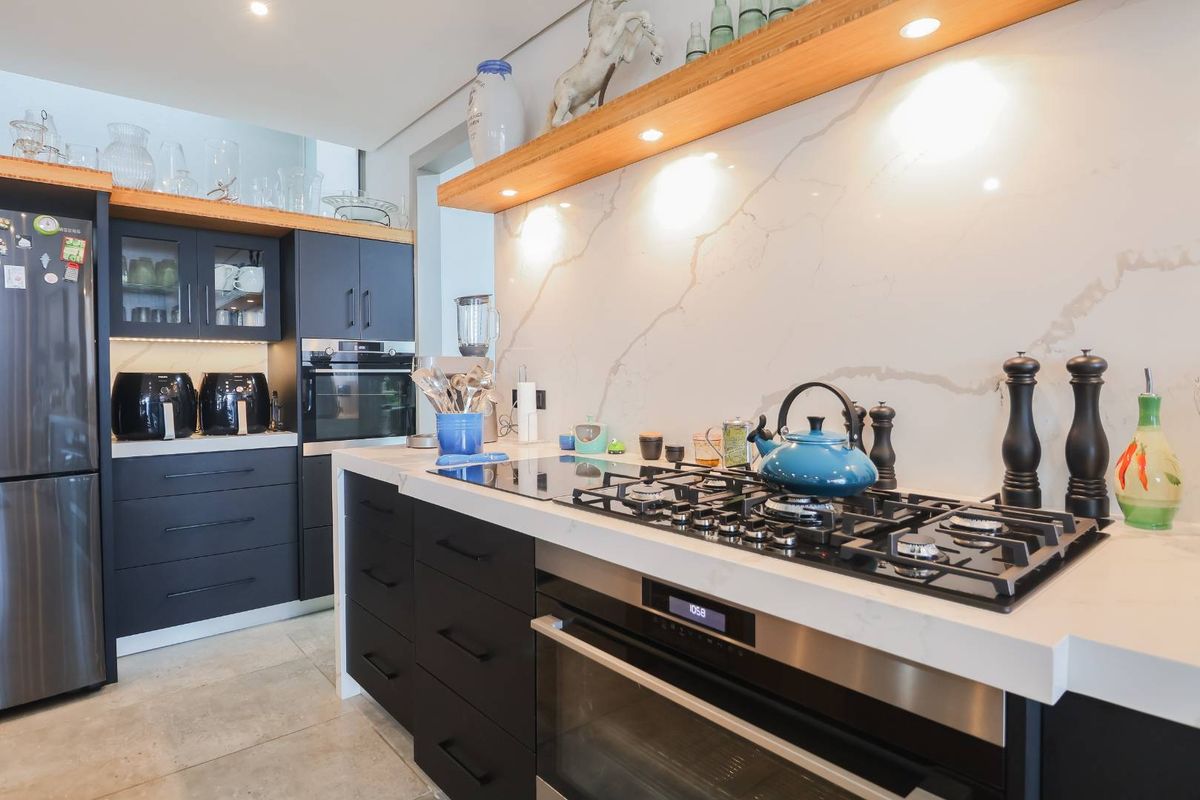Modern kitchen featuring dark cabinetry, stone countertops, integrated oven, gas cooktop, and a marble-look splashback with feature timber shelving.