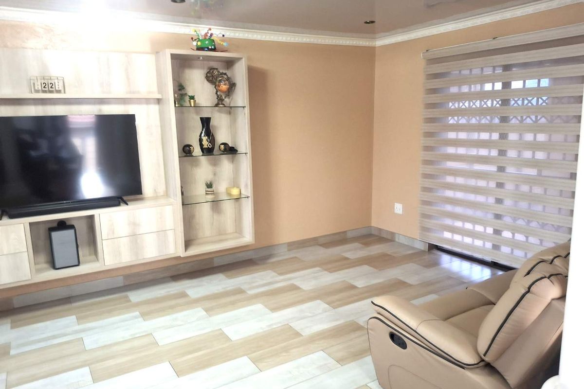 A living room featuring a built-in media unit, recessed ceiling lighting, decorative coving, and modern wood-look tiled flooring.