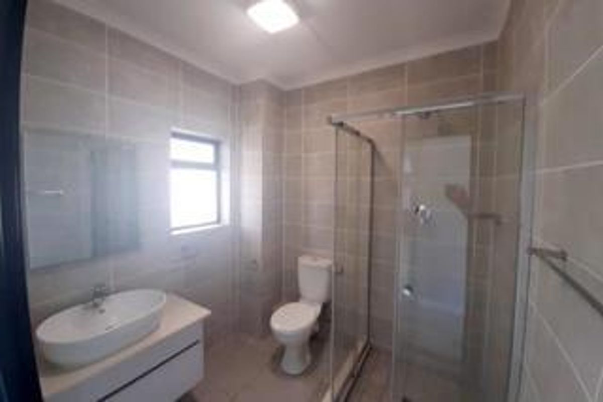 A modern bathroom featuring a glass-enclosed shower, a wall-mounted vanity with a basin, and neutral floor-to-ceiling wall tiles.