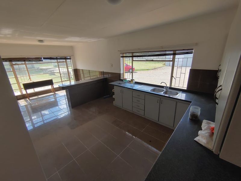 Spacious open-plan kitchen and living area featuring tiled flooring, built-in cabinetry, a breakfast bar, and large windows with security bars.
