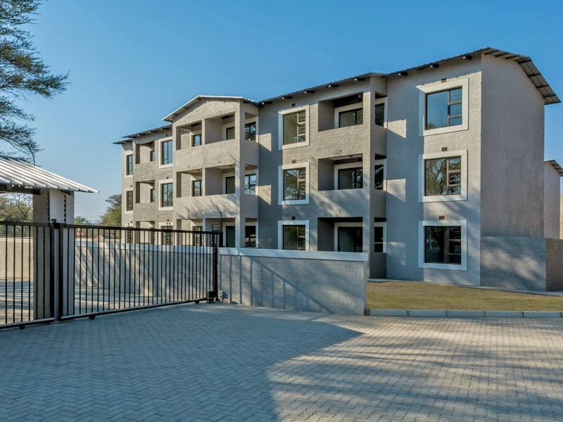 A modern multi-story apartment complex featuring a paved driveway, secure gated entrance, and well-maintained exterior facade with private balconies.