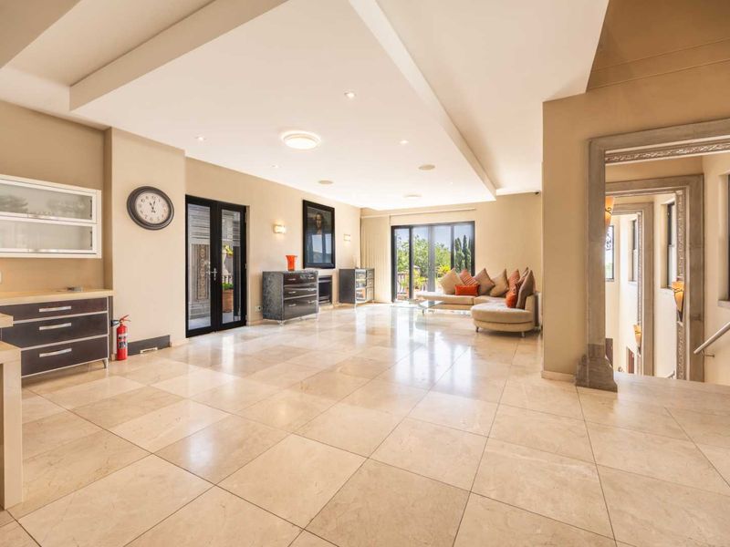 Spacious open-plan living area featuring polished travertine flooring, a coffered ceiling with recessed lighting, and seamless access to an outdoor patio.